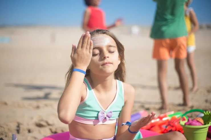 Bimba che mette la crema solare in spiaggia