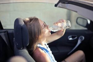 Donna accaldata in macchina che beve acqua